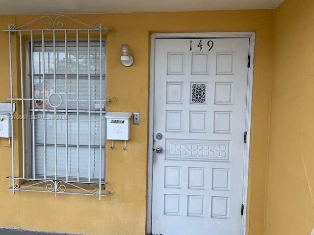 An exterior view of a yellow wall with a white door and a barred window — 149 Bentley Dr # 149A, Miami Springs FL 33166, MIAMI SPRINGS, FL