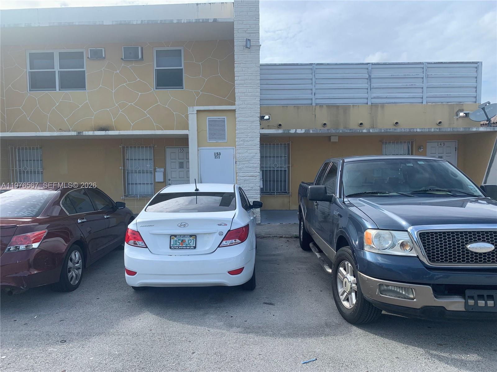 A two-story building exterior features yellow stucco walls, a white brick column, and parking spaces — 149 Bentley Dr # 149A, Miami Springs FL 33166, MIAMI SPRINGS, FL