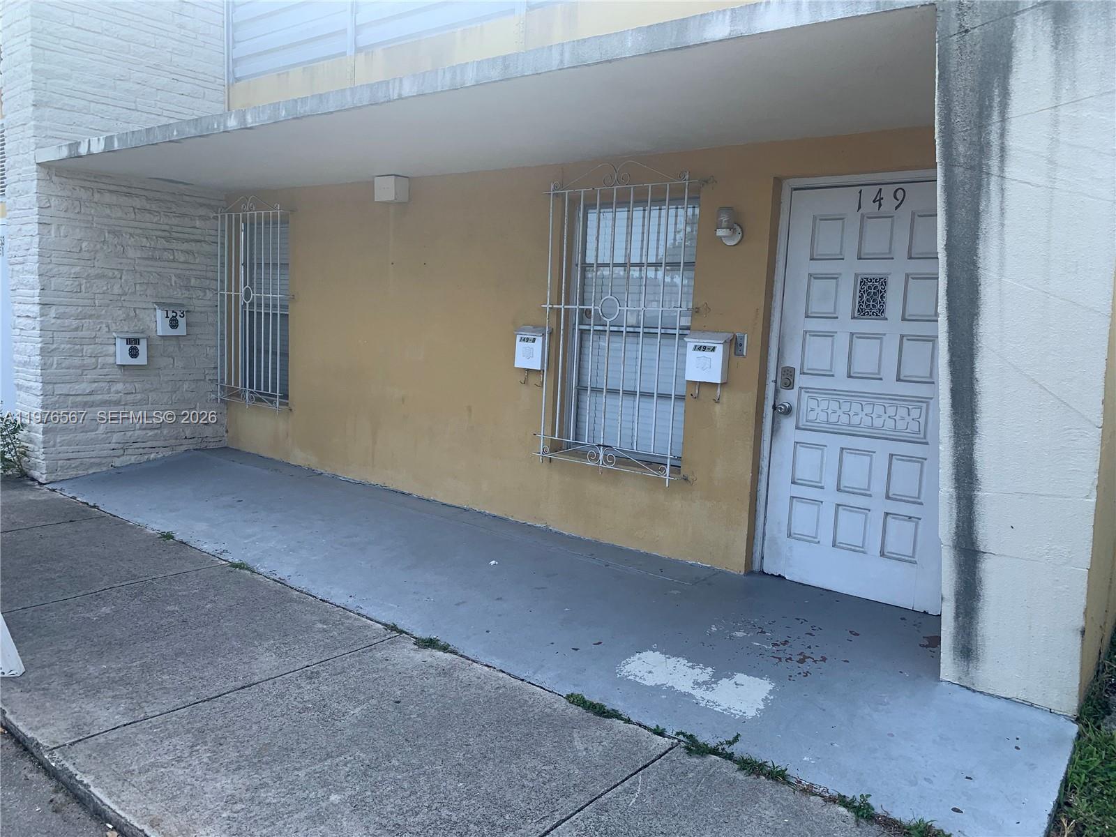An exterior view of a building entrance with a white door and metal window grates — 149 Bentley Dr # 149A, Miami Springs FL 33166, MIAMI SPRINGS, FL