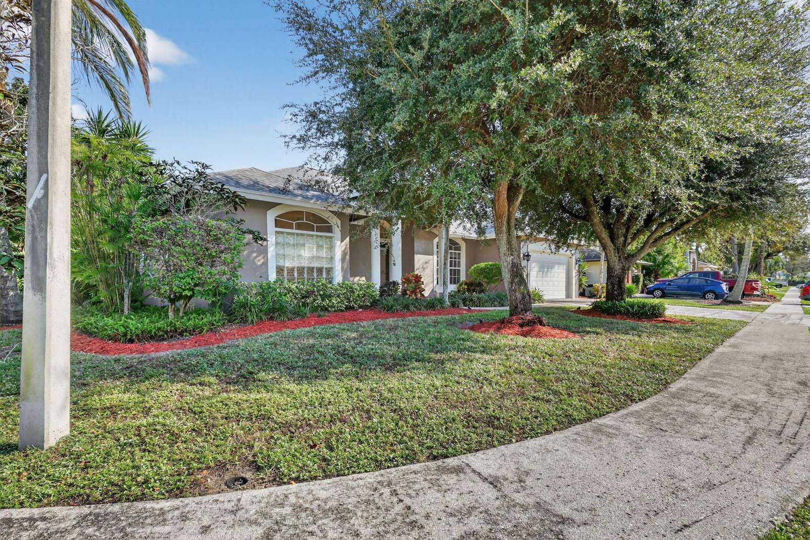 A single-story house with a tan exterior, arched windows, and a large tree in front — 1500 Firethorn Drive, Wellington FL 33414, WELLINGTON, FL