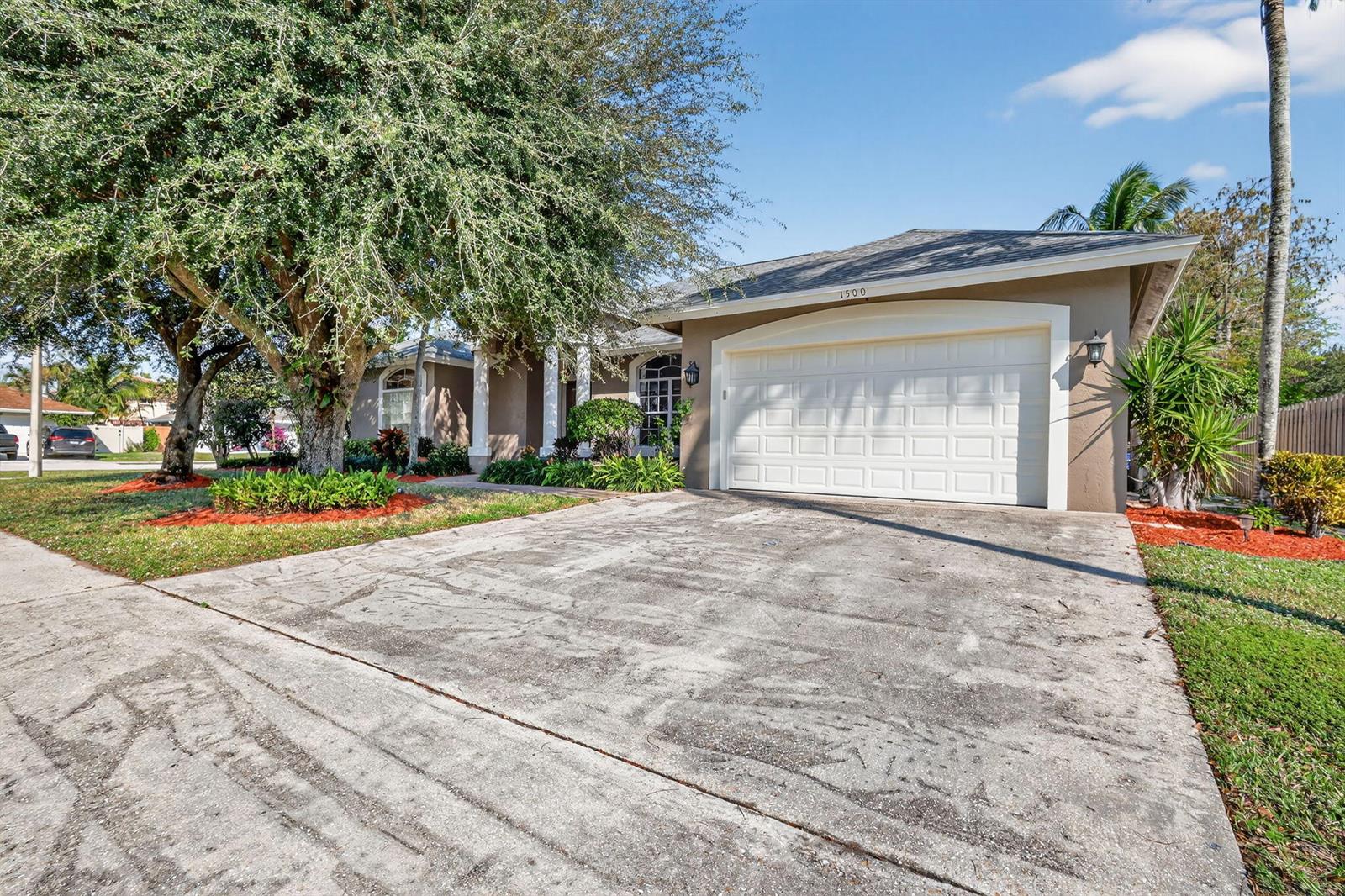 A single-story house with a beige exterior, a two-car garage, and a large shade tree — 1500 Firethorn Drive, Wellington FL 33414, WELLINGTON, FL