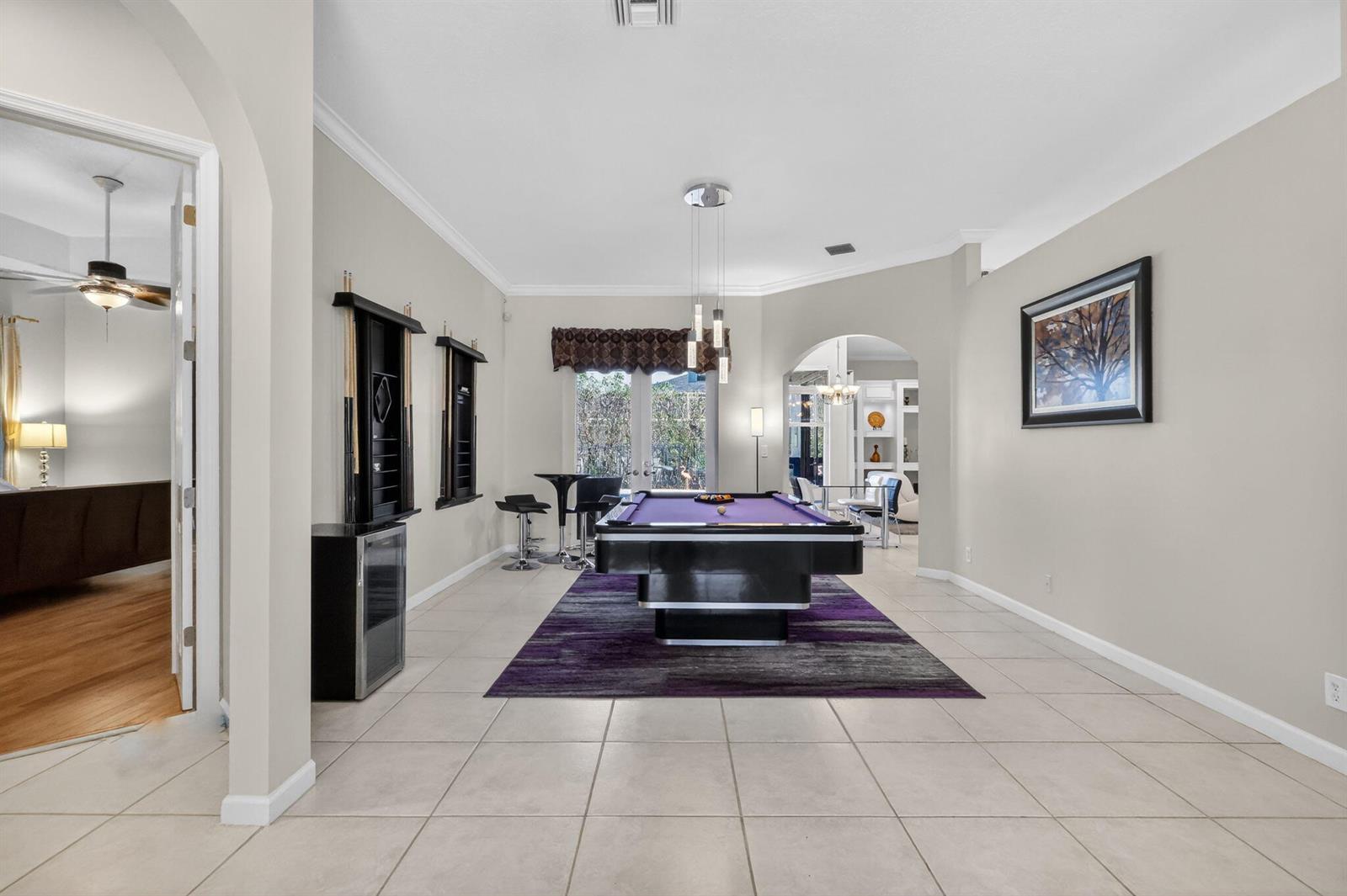 A game room features a purple pool table on a rug, tile flooring, and bar seating — 1500 Firethorn Drive, Wellington FL 33414, WELLINGTON, FL