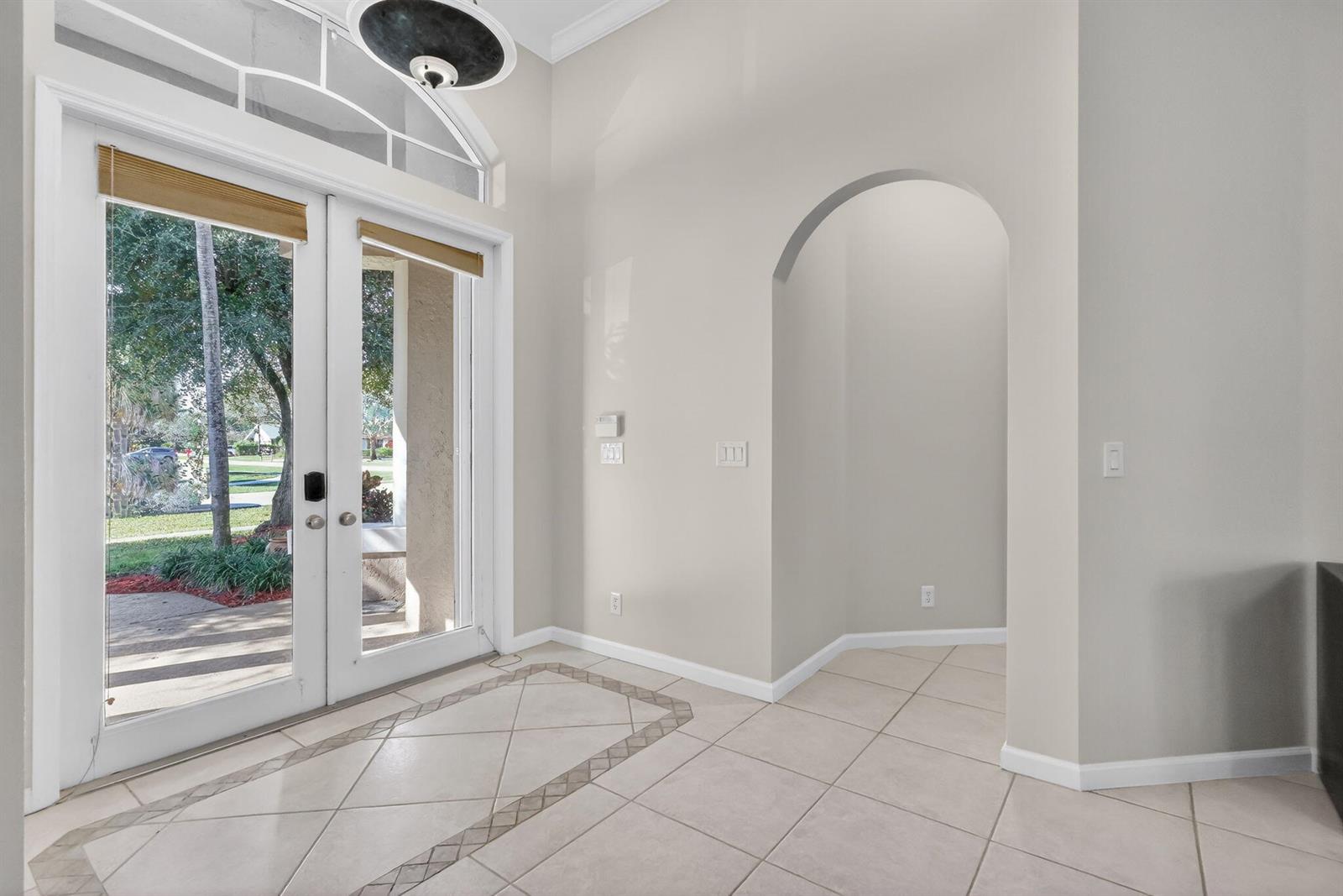 An entryway features tile flooring, an arched doorway, and double glass doors with a transom — 1500 Firethorn Drive, Wellington FL 33414, WELLINGTON, FL