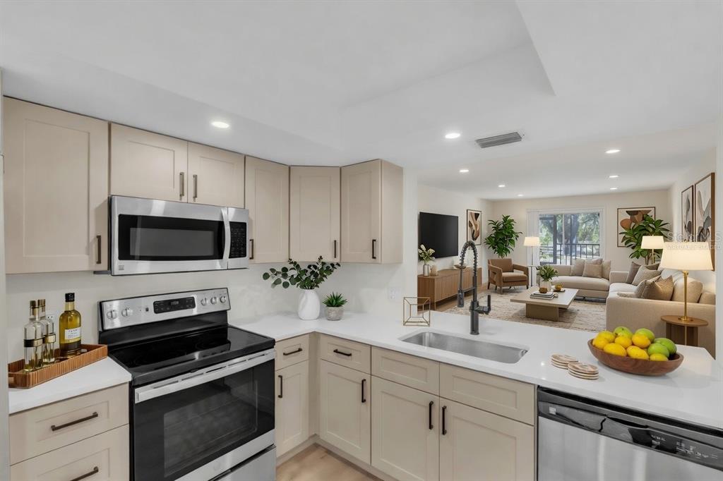 A modern kitchen with light-colored cabinets, stainless steel appliances, and a view into the living room — 6304 POINTE WEST BOULEVARD UNIT A107, BRADENTON, FL