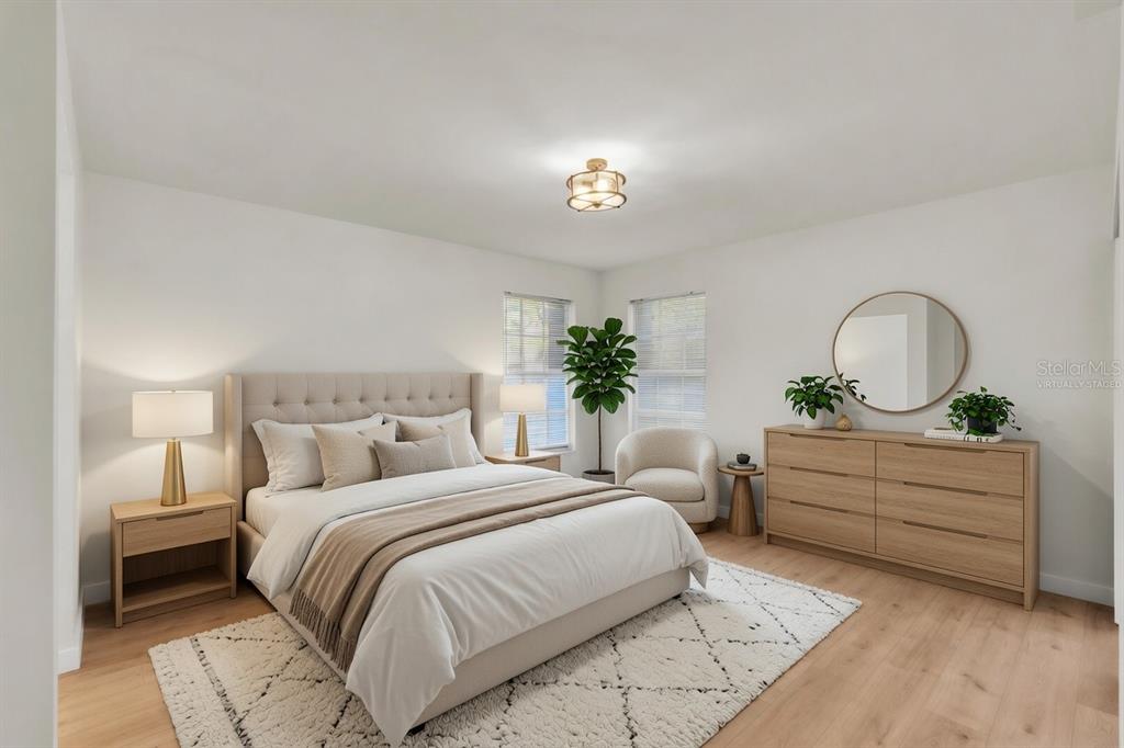 A virtually staged bedroom features a tufted bed, light wood furniture, and a round mirror — 6304 POINTE WEST BOULEVARD UNIT A107, BRADENTON, FL
