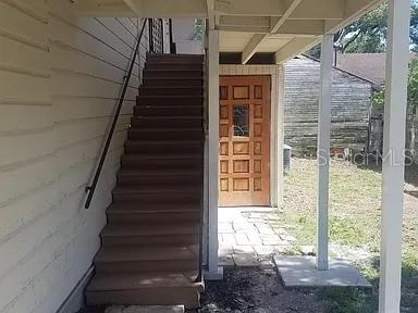 An exterior view shows a wooden staircase leading to an upper level beside a paneled door — 114 W WILDER AVENUE, TAMPA, FL