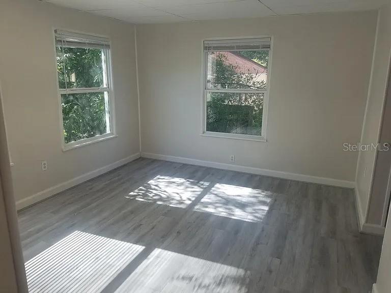 An empty room features light gray wood-look flooring, neutral walls, and two windows — 114 W WILDER AVENUE, TAMPA, FL