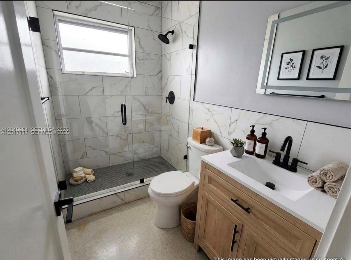 A bathroom features a glass-enclosed shower, a wood vanity with a white sink, and marble-look tiles — 1140 NE 24th Ave # 1, Pompano Beach FL 33062, POMPANO BEACH, FL
