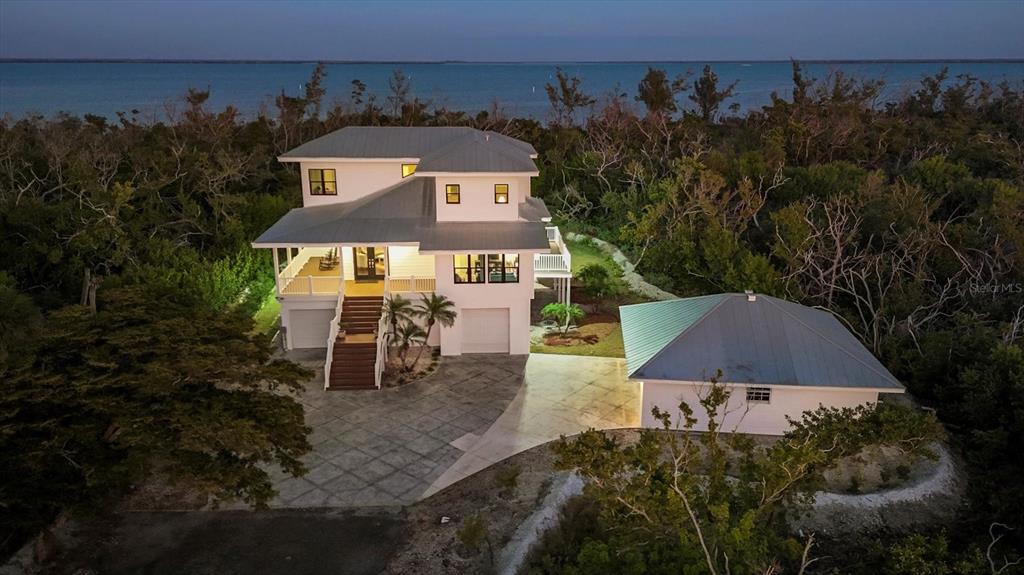 An elevated two-story white house with a metal roof sits near a body of water — 5010 GROUPER HOLE COURT, BOCA GRANDE, FL