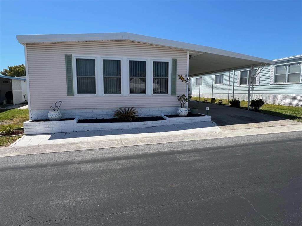 A single-story manufactured home with light siding, a white brick planter, and an attached carport — 825 COCONUT PALM STREET, LARGO, FL