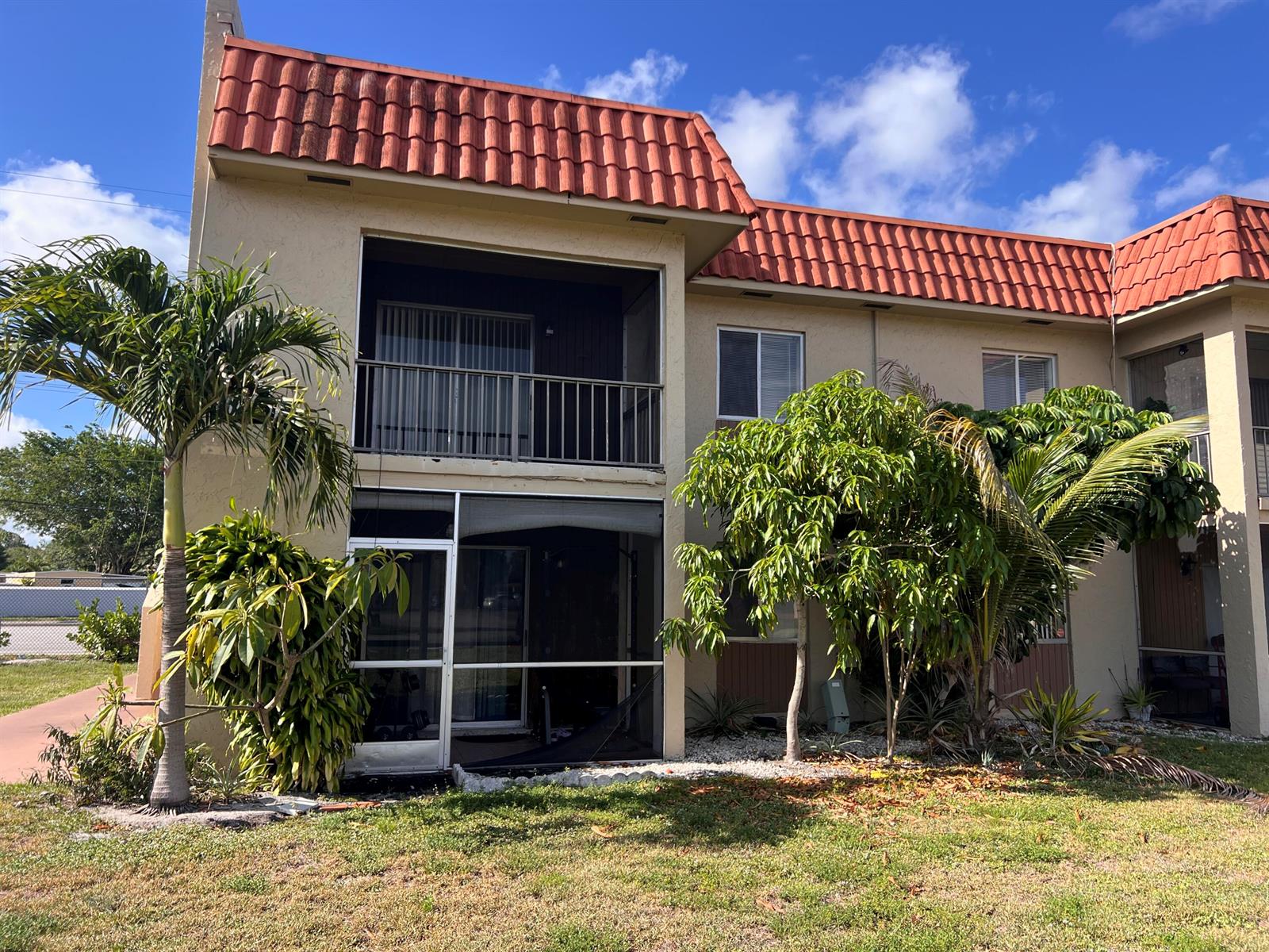 A two-story apartment building features a red tile roof, stucco exterior, and screened-in balconies — 6034 Forest Hill Boulevard # 209, West Palm Beach FL 33415, WEST PALM BEACH, FL
