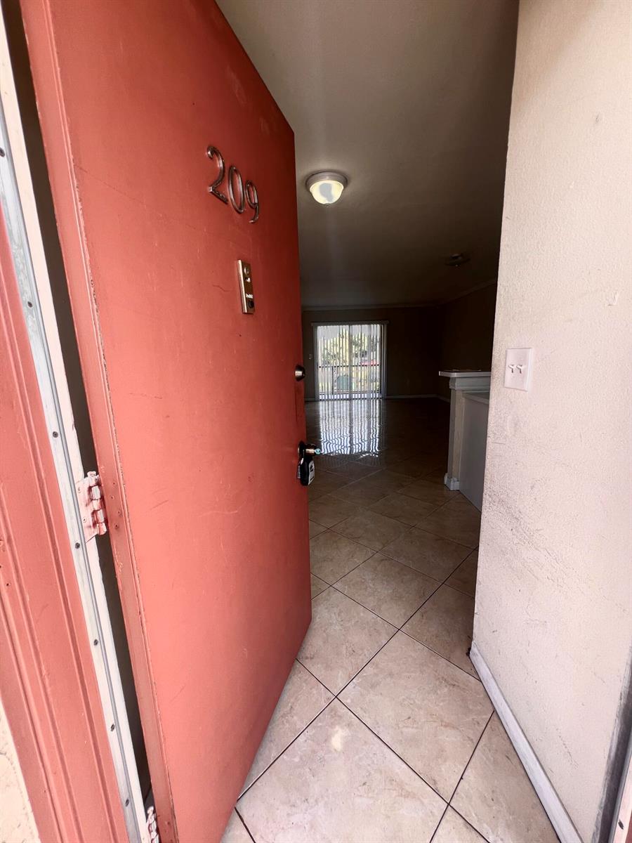 An open red door reveals a tiled entryway leading into a living area with sliding doors — 6034 Forest Hill Boulevard # 209, West Palm Beach FL 33415, WEST PALM BEACH, FL