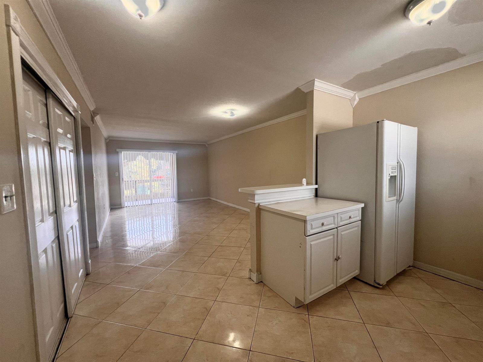 An open-concept living area features beige tile flooring, a white kitchen cabinet, and a refrigerator — 6034 Forest Hill Boulevard # 209, West Palm Beach FL 33415, WEST PALM BEACH, FL