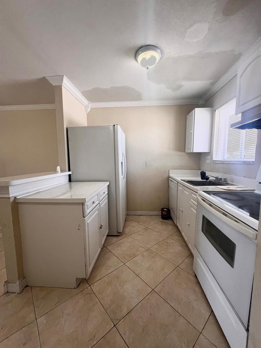 A kitchen features white cabinets, a refrigerator, a stove, and tile flooring — 6034 Forest Hill Boulevard # 209, West Palm Beach FL 33415, WEST PALM BEACH, FL