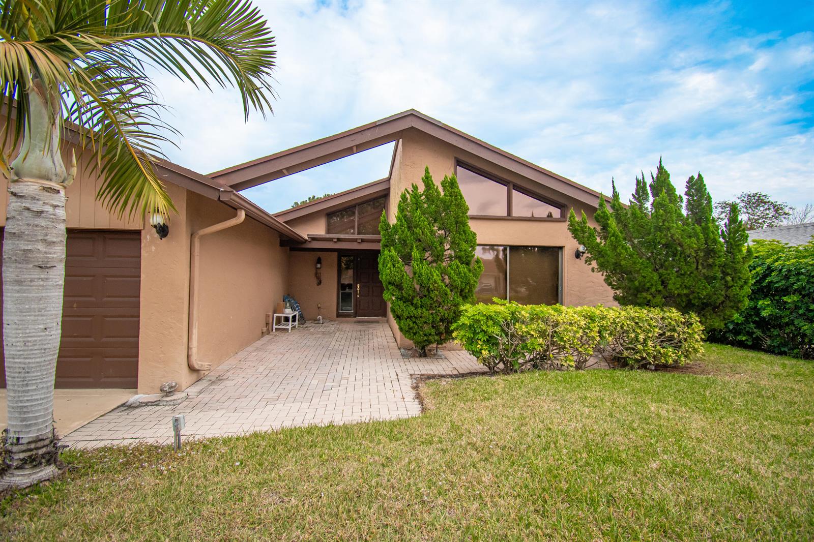 A tan single-story house features a paved walkway, a brown garage door, and large windows — 21566 Arbor Way, Boca Raton FL 33433, BOCA RATON, FL