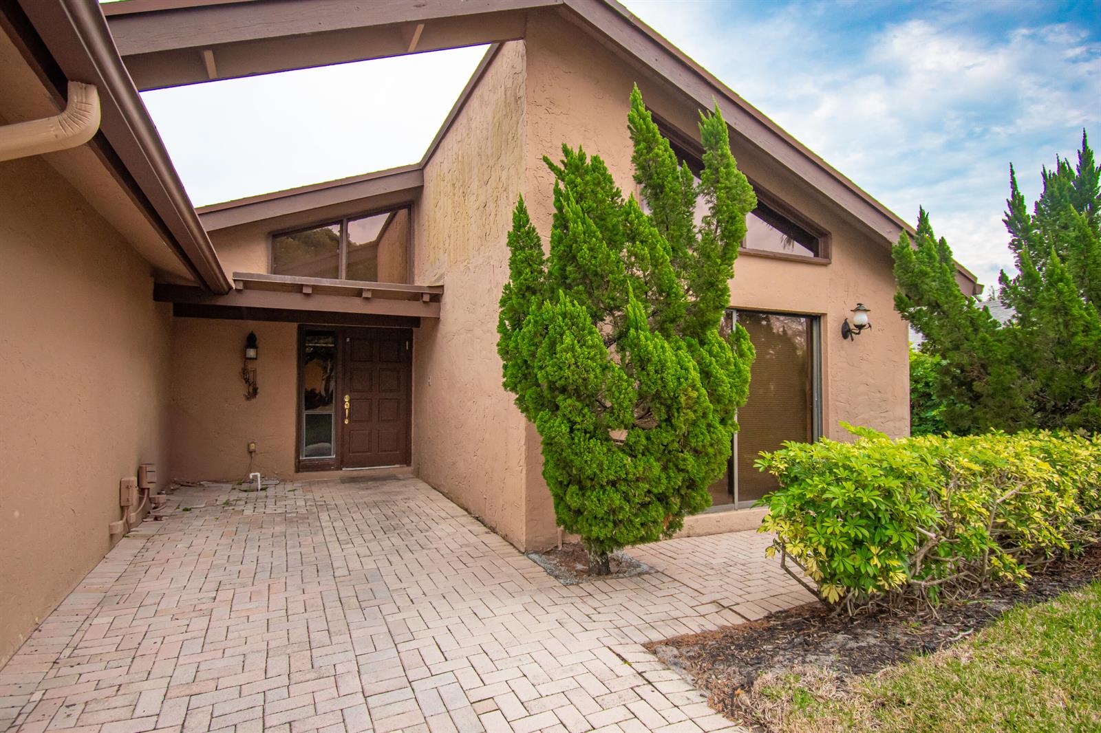 A tan stucco house features a brick paver entryway, a brown front door, and landscaping — 21566 Arbor Way, Boca Raton FL 33433, BOCA RATON, FL