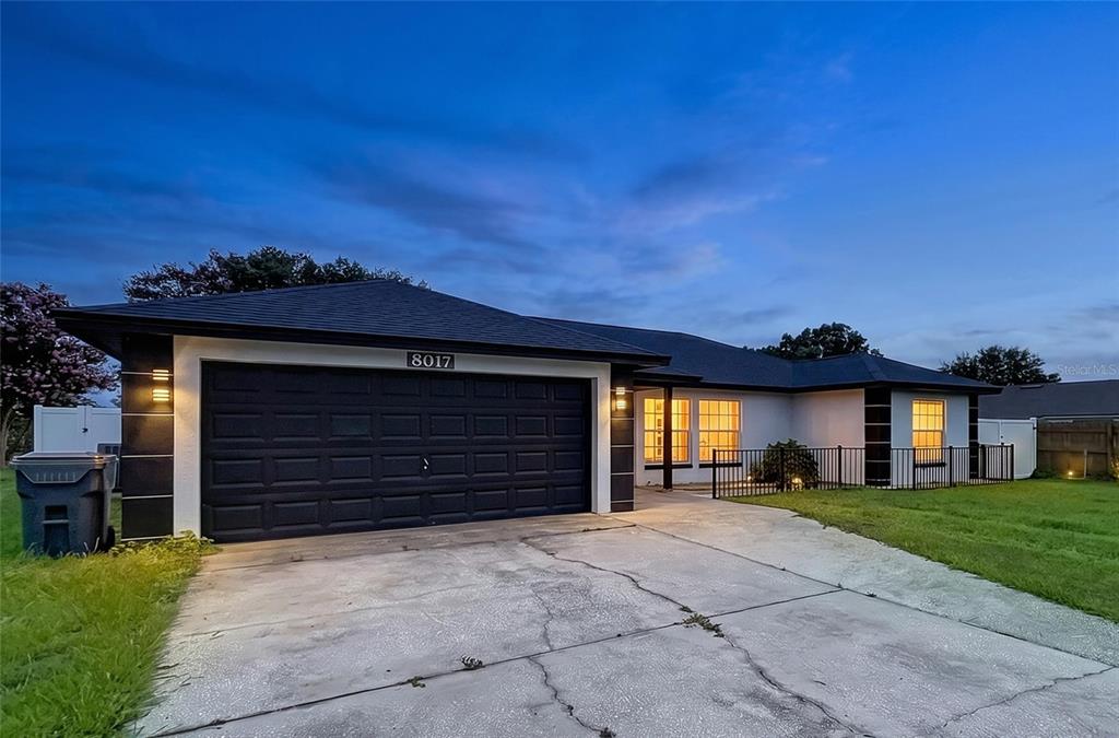 A single-story house with a black garage door and white exterior walls at dusk — 8017 GLENRIDGE LANE, LAKELAND, FL