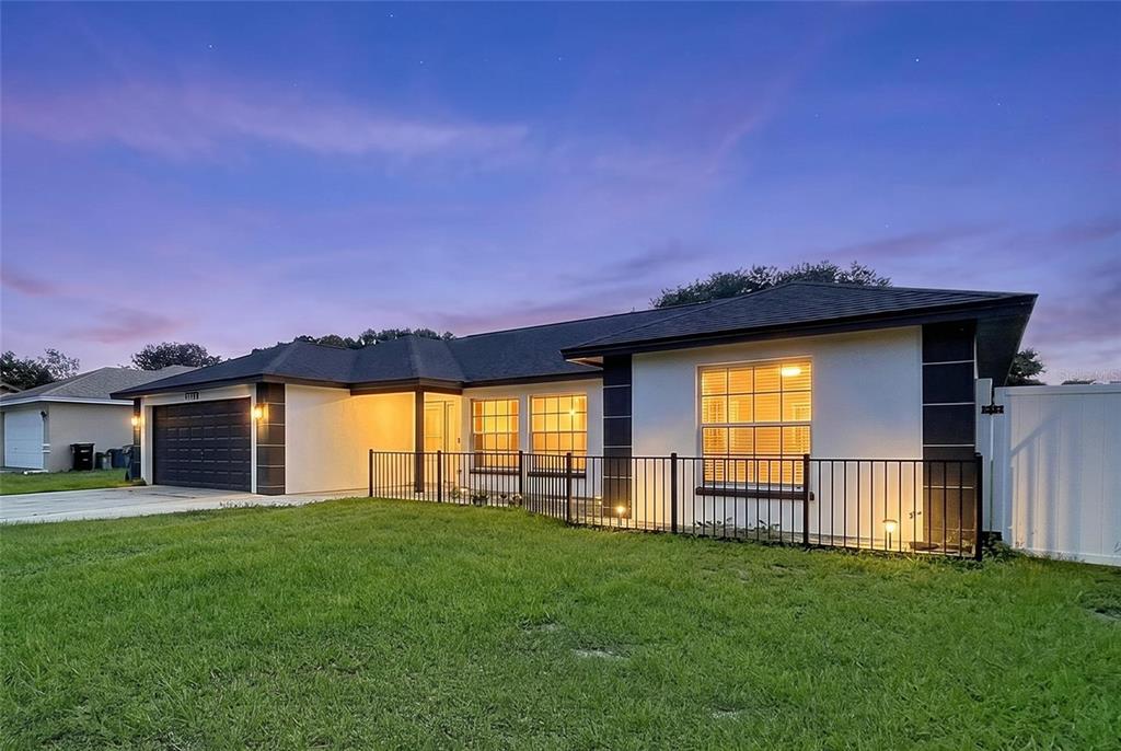 A single-story house with a dark roof, white stucco walls, and a black metal fence — 8017 GLENRIDGE LANE, LAKELAND, FL