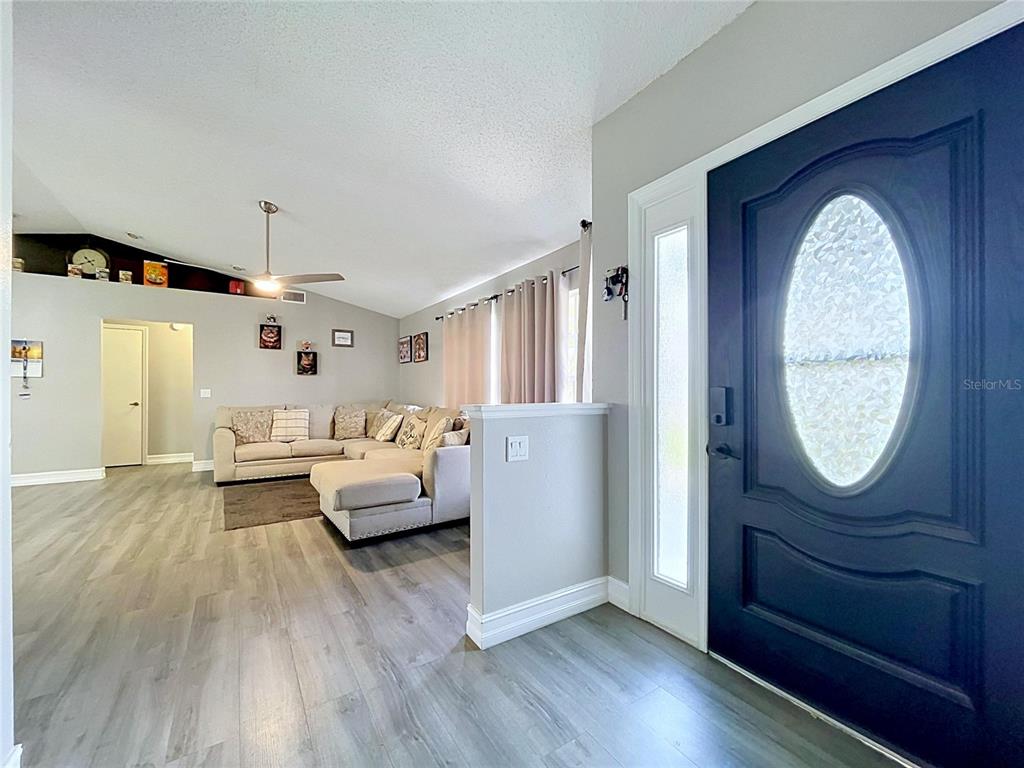 A view of a living room with light wood flooring and a dark blue front door — 8017 GLENRIDGE LANE, LAKELAND, FL