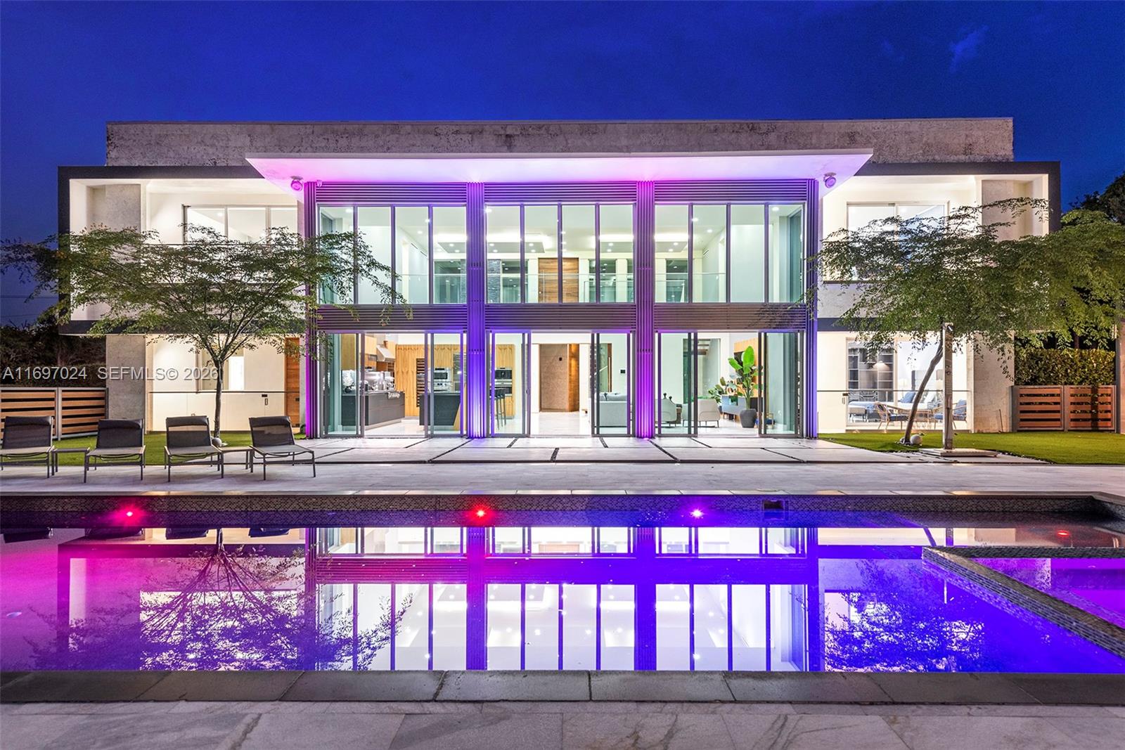 A modern two-story house with floor-to-ceiling windows and purple accent lighting overlooks a swimming pool — 14305 Stirling Rd, Southwest Ranches FL 33330, SOUTHWEST RANCHES, FL