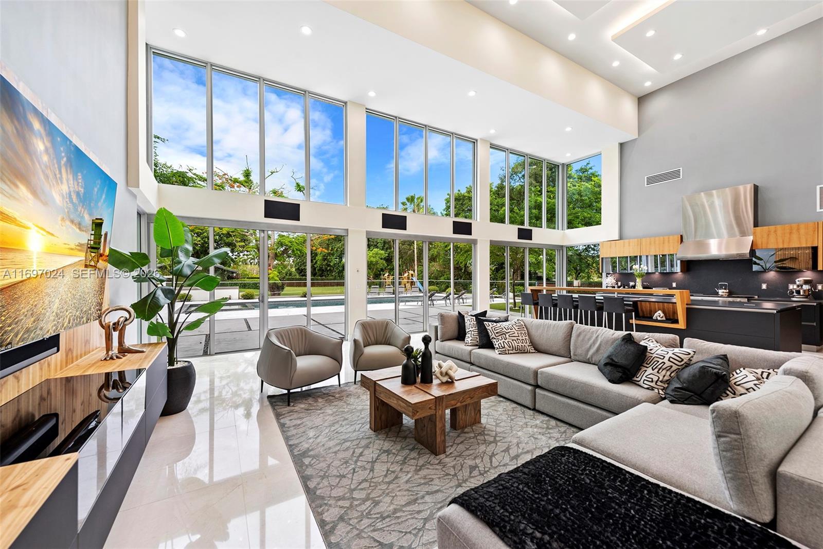 A modern living room with floor-to-ceiling windows, a large sectional sofa, and an open kitchen — 14305 Stirling Rd, Southwest Ranches FL 33330, SOUTHWEST RANCHES, FL