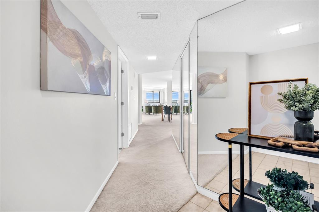 A carpeted hallway leads to a living area, featuring a mirrored wall and console table — 1651 SAND KEY ESTATES CT UNIT 74, CLEARWATER BEACH, FL