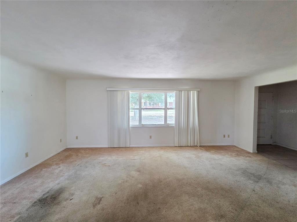 An empty living room features white walls, a large window with vertical blinds, and carpet — 416 6TH ST S, DUNDEE, FL