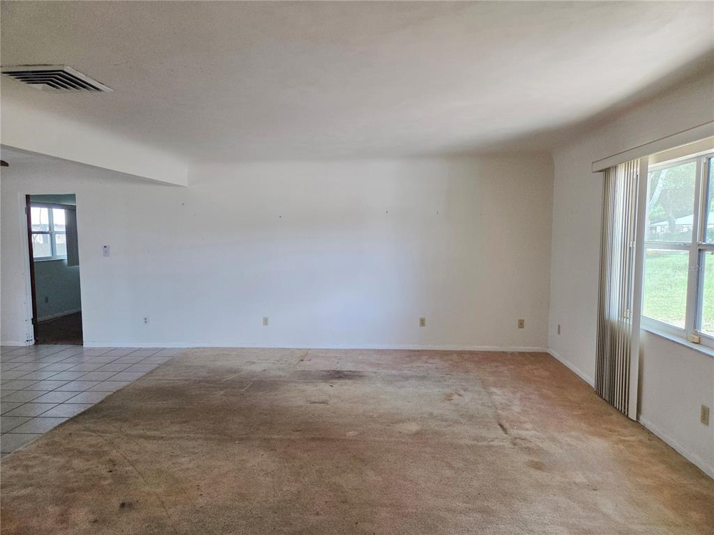 An empty living room features beige wall-to-wall carpeting, white walls, and a large window — 416 6TH ST S, DUNDEE, FL