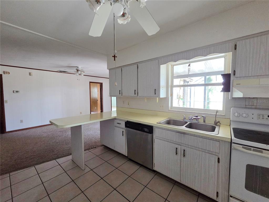 A kitchen features white cabinets, a stainless steel dishwasher, a double sink, and tile flooring — 416 6TH ST S, DUNDEE, FL