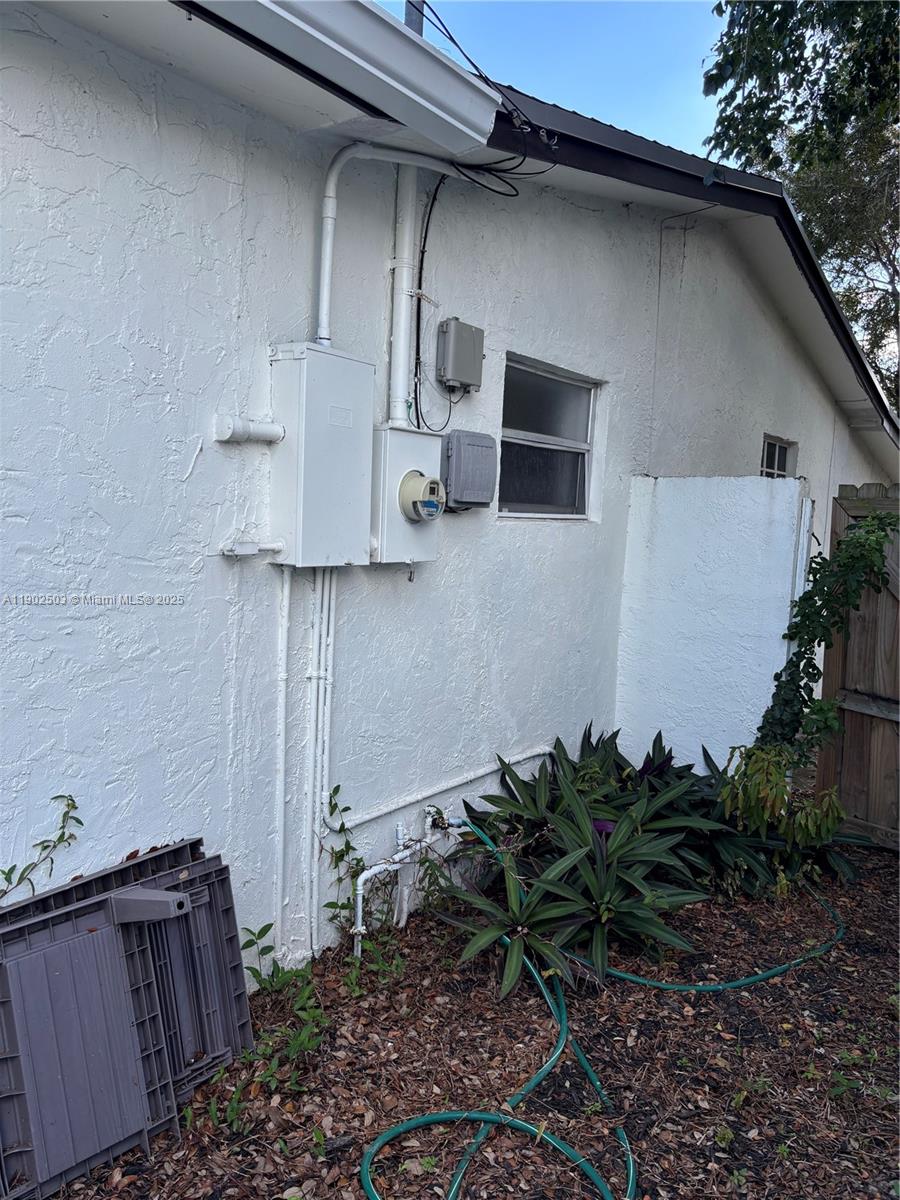 The exterior wall of a house features an electrical meter, utility boxes, and landscaping — 6541 Sherman St, Hollywood FL 33024, HOLLYWOOD, FL