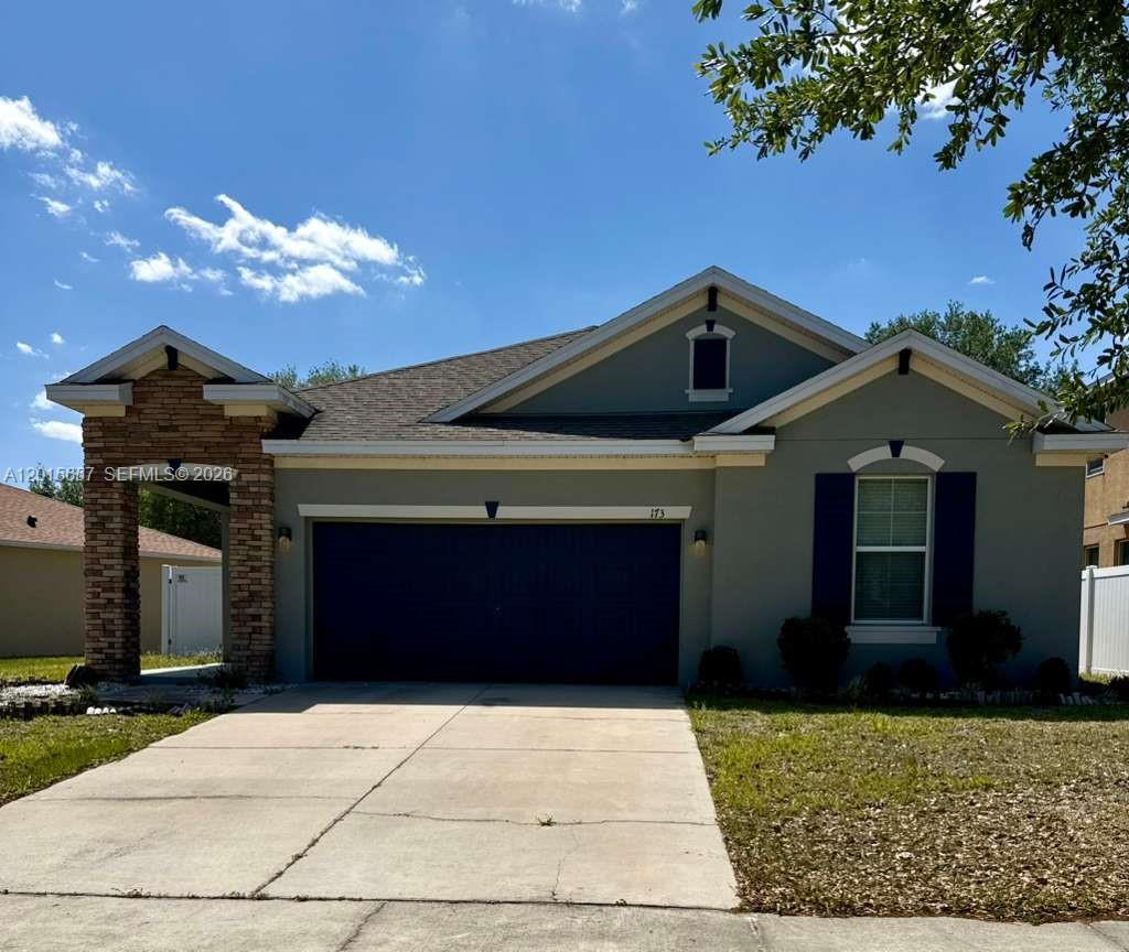 A single-story suburban house features a stone-accented entryway, a two-car garage, and gray siding — 173 Tracy Circle, Winter Haven FL 33884, WINTER HAVEN, FL