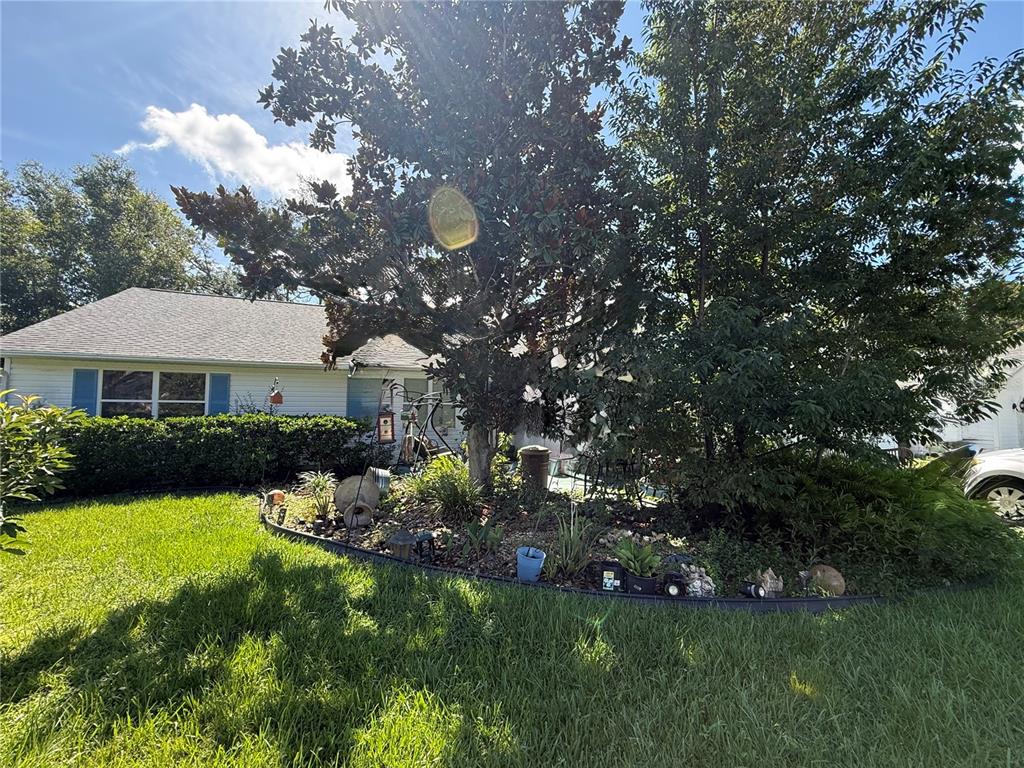 A large tree and landscaped garden bed sit in the front yard of a house — 1117 BEN HOPE DRIVE, LEESBURG, FL