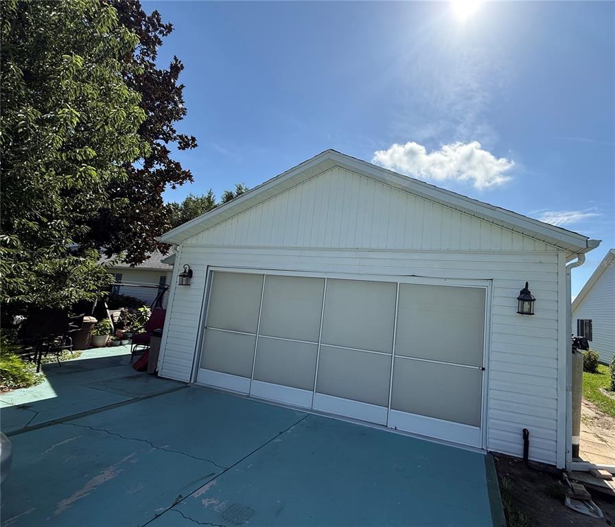 A white detached garage with a large sliding screen door sits on a painted concrete driveway — 1117 BEN HOPE DRIVE, LEESBURG, FL