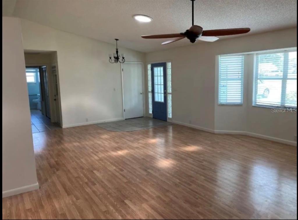 A living room with light wood flooring, a ceiling fan, and a blue front door — 1117 BEN HOPE DRIVE, LEESBURG, FL