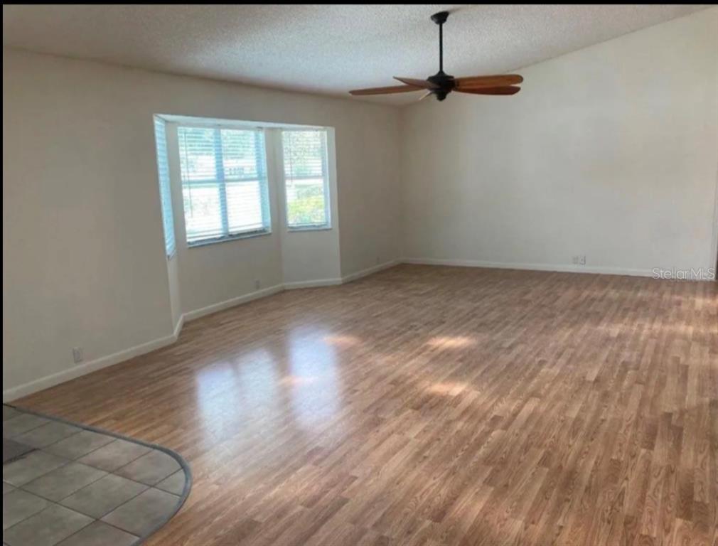 An empty living room features light wood-look flooring, a ceiling fan, and a bay window — 1117 BEN HOPE DRIVE, LEESBURG, FL