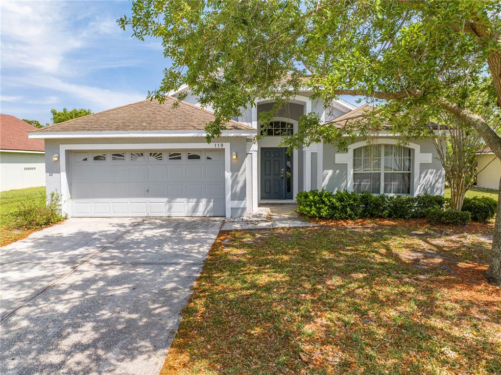 A single-story house with a gray garage, dark front door, and a large tree in front — 119 SOUTHAMPTON DRIVE, KISSIMMEE, FL