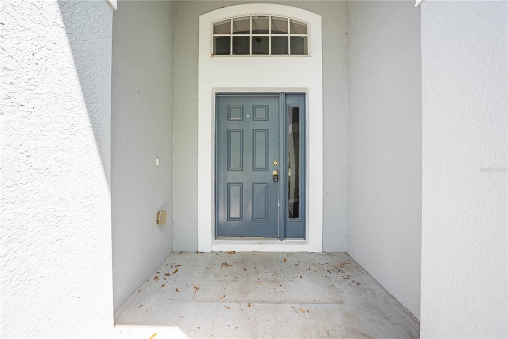 A blue front door with a sidelight and arched transom window sits under a covered entryway — 119 SOUTHAMPTON DRIVE, KISSIMMEE, FL