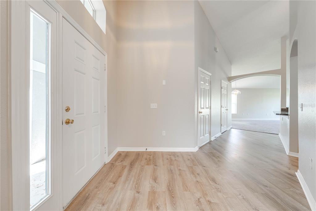 A bright entryway features light wood-look flooring, white doors, and a vaulted ceiling — 119 SOUTHAMPTON DRIVE, KISSIMMEE, FL