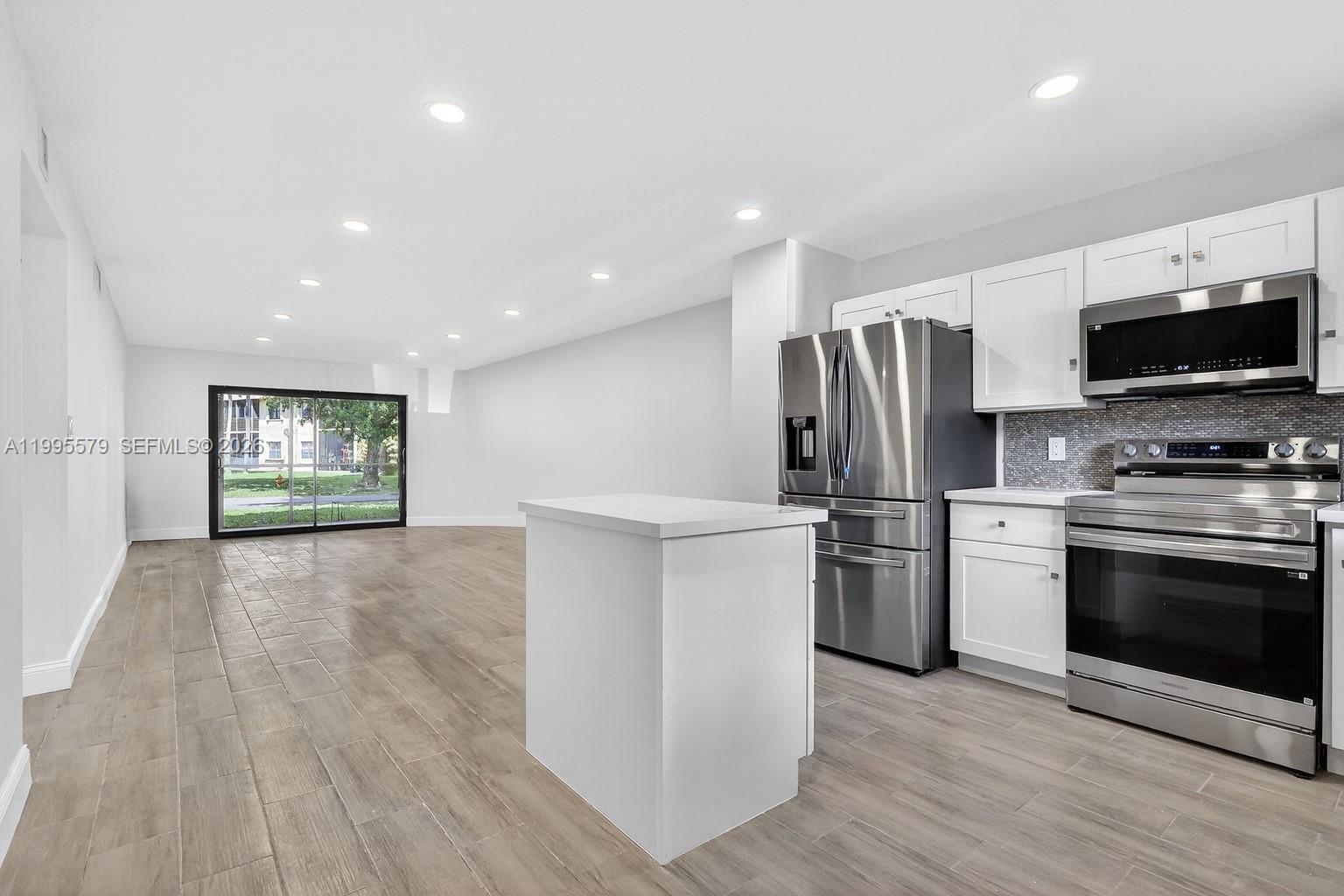 A kitchen with white cabinets and stainless steel appliances opens into a living area — 275 Gate Rd # 104, Hollywood FL 33024, HOLLYWOOD, FL