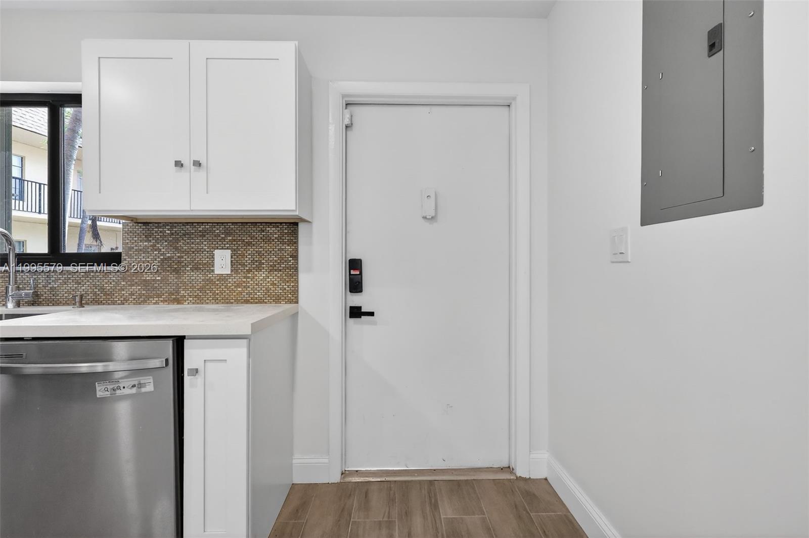 A kitchen area features white cabinets, a mosaic tile backsplash, and a white entry door — 275 Gate Rd # 104, Hollywood FL 33024, HOLLYWOOD, FL