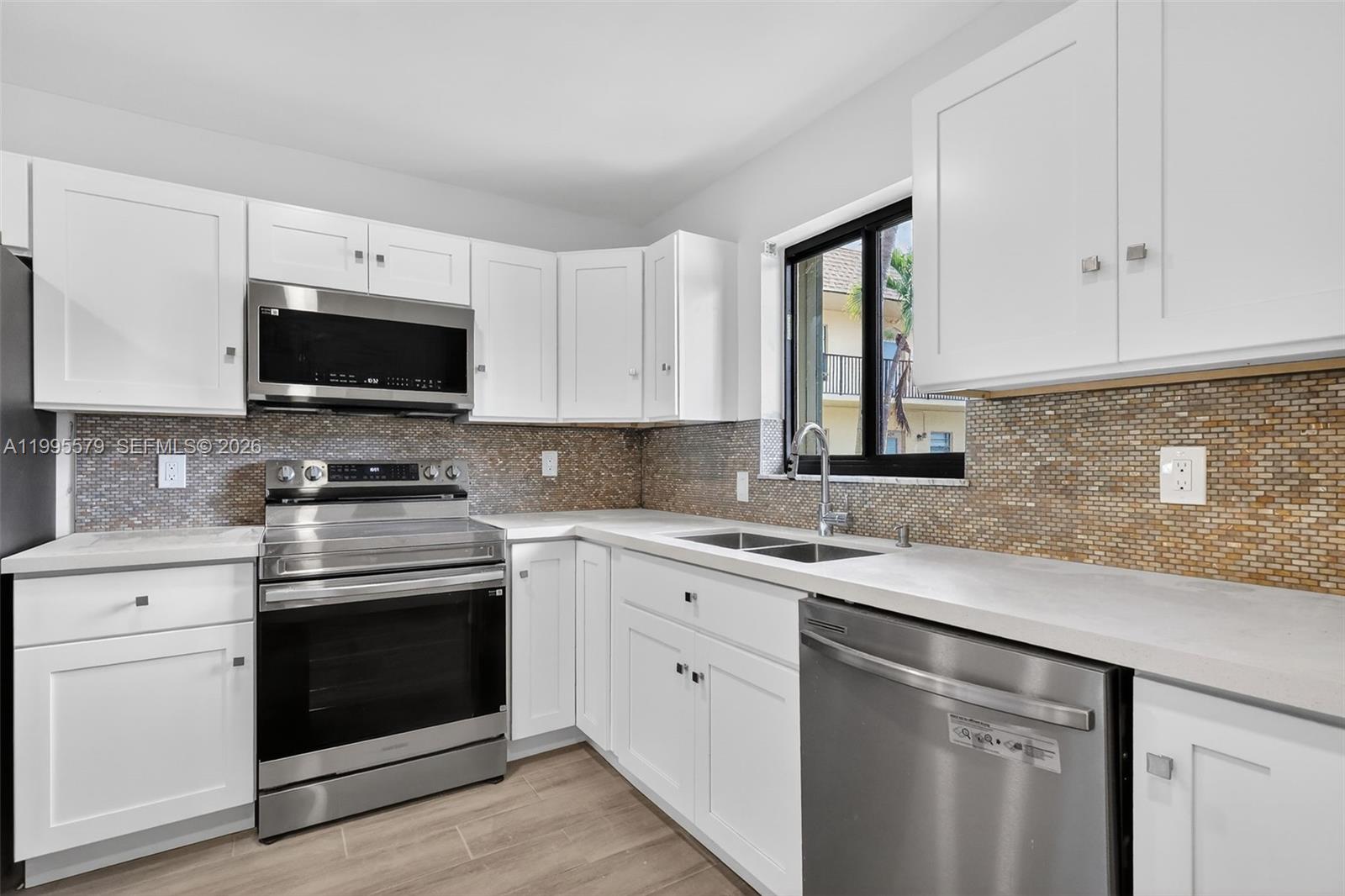 A kitchen features white cabinets, stainless steel appliances, a tiled backsplash, and light countertops — 275 Gate Rd # 104, Hollywood FL 33024, HOLLYWOOD, FL