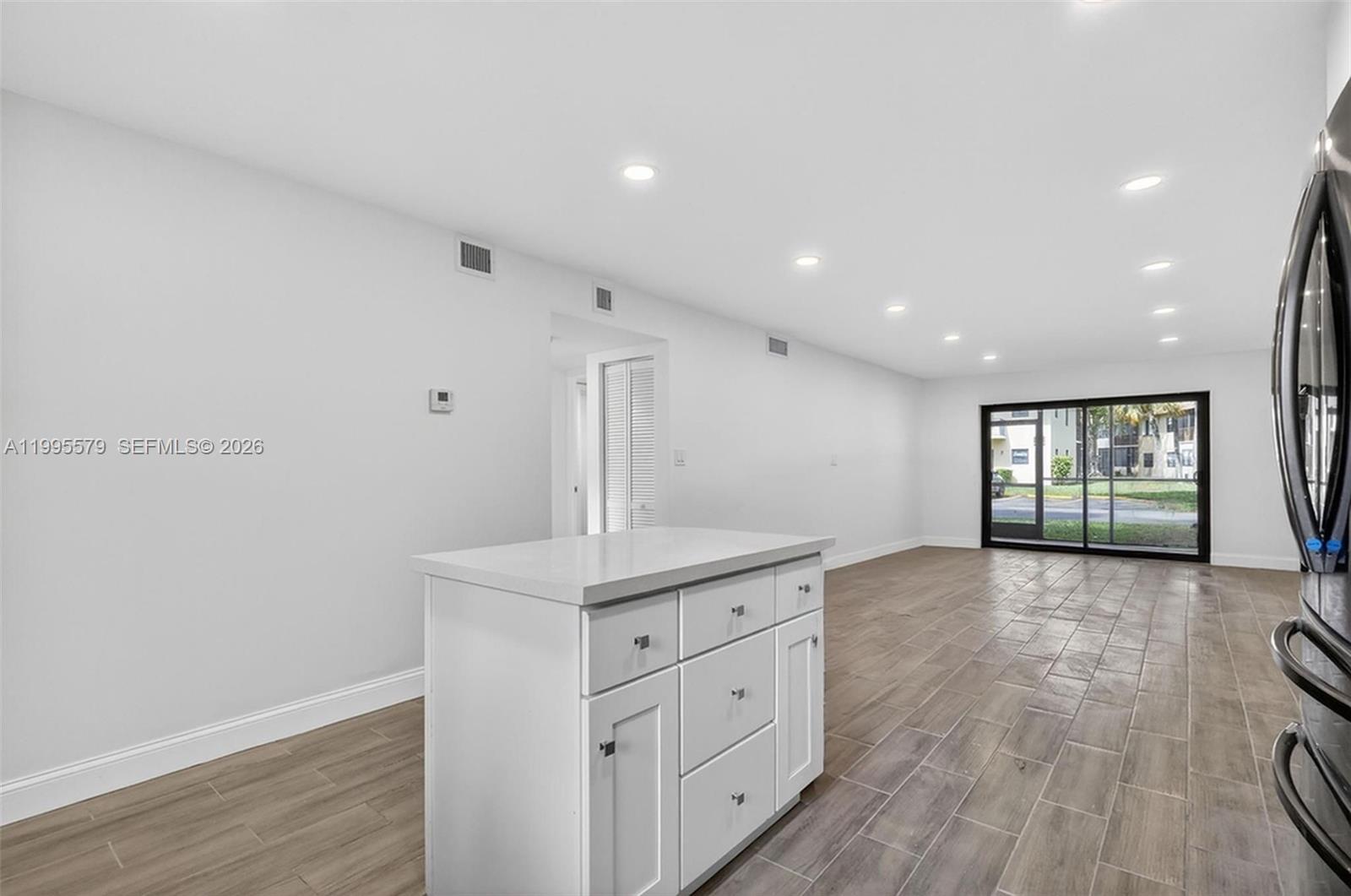 A white kitchen island sits in an open-concept room with wood-look tile flooring — 275 Gate Rd # 104, Hollywood FL 33024, HOLLYWOOD, FL