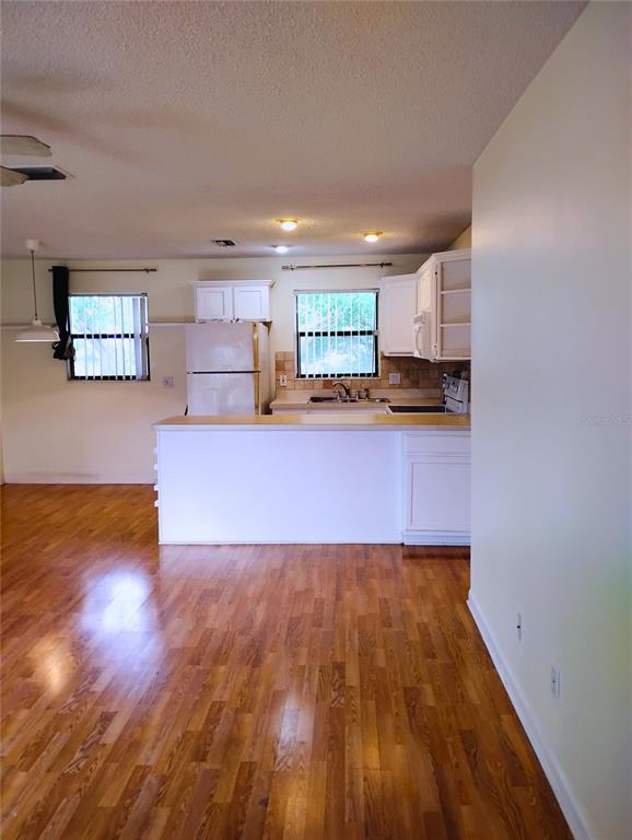A kitchen with white cabinets and a breakfast bar overlooks a room with wood flooring — 4973 91ST AVENUE UNIT 12 (C), PINELLAS PARK, FL