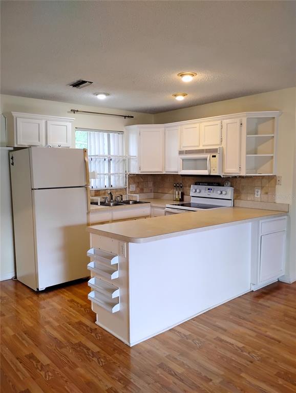 A kitchen with white cabinets, a white refrigerator, and a peninsula counter on wood flooring — 4973 91ST AVENUE UNIT 12 (C), PINELLAS PARK, FL