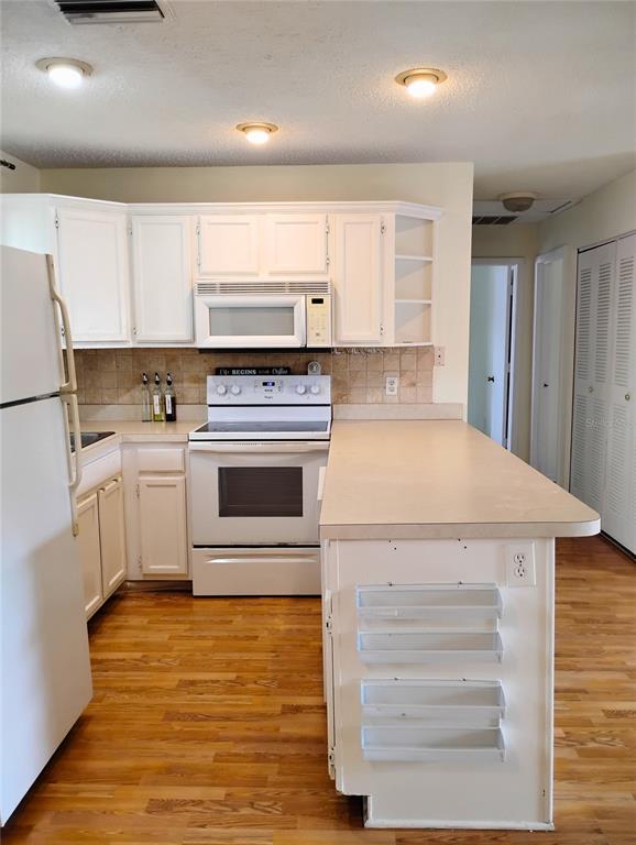 A kitchen with white cabinets, white appliances, a peninsula, and hardwood flooring — 4973 91ST AVENUE UNIT 12 (C), PINELLAS PARK, FL