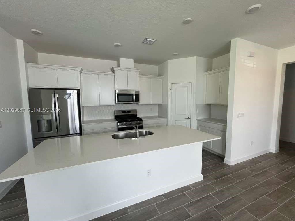 A modern kitchen features white cabinetry, stainless steel appliances, and a large quartz island — 19788 Whispering Creek Rd # 19788, Loxahatchee FL 33470, LOXAHATCHEE, FL