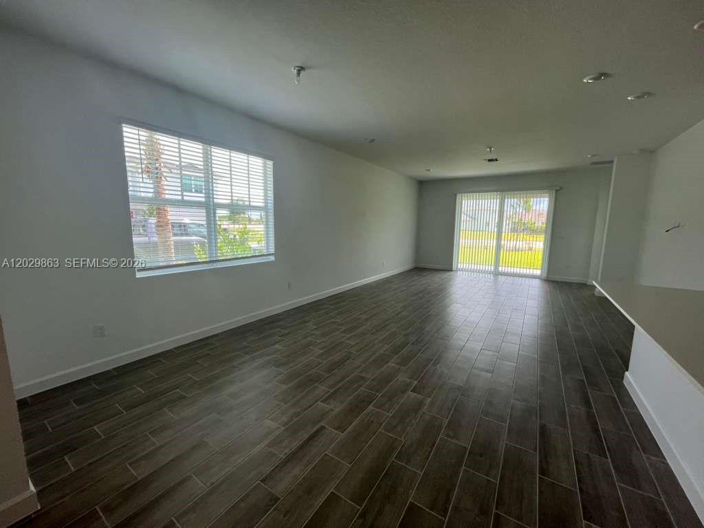 An empty living area features dark wood-look tile flooring, white walls, and a sliding glass door — 19788 Whispering Creek Rd # 19788, Loxahatchee FL 33470, LOXAHATCHEE, FL