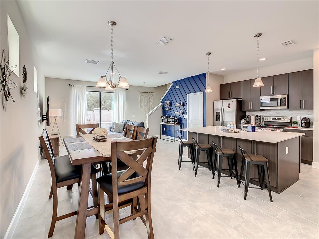 An open-concept kitchen and dining area features dark wood cabinetry, a large island, and tile flooring — 208 VILLA DOMANI CIRCLE, DAVENPORT, FL