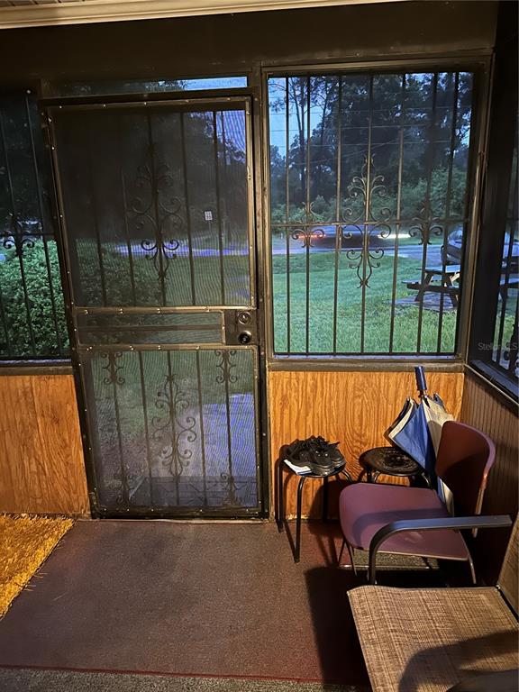 A screened-in porch features wood-paneled walls, a metal security door, and a view of outdoors — 14787 SE 36TH AVENUE, SUMMERFIELD, FL