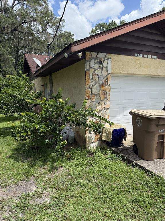 The exterior of a house features a stone-accented wall, a garage door, and a trash bin — 14787 SE 36TH AVENUE, SUMMERFIELD, FL